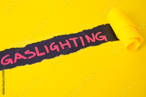 Black surface, with word gaslighting in red. Underneath torn yellow cardboard. 