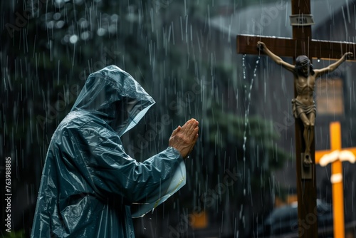 person in raincoat praying by cross during a downpour