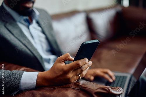 Close up of black businessman using cell phone while working on laptop.