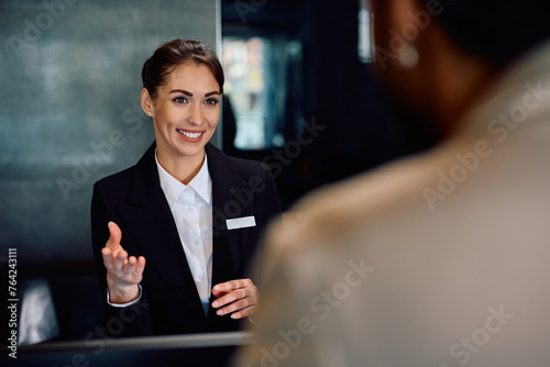 Happy hotel manager talking to guest at reception desk.