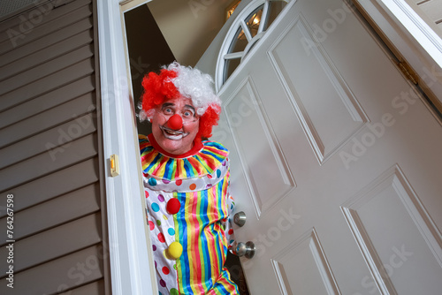 Awkward creepy man dressed in a clown costume answering the door during Halloween