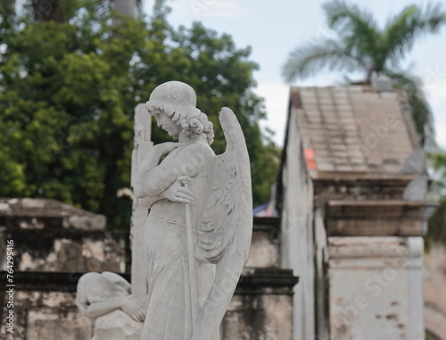 Marble Resurrection Angel with crossed arms holding a trumpet and strapless robe, topping a tomb in the Cementerio de Colon Cemetery. Havana-Cuba-096