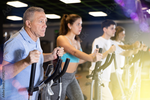 Group of athletic people of different ages train on elliptical trainers steppers