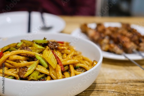 Goshilik lagman, a Uyghur dish of fresh handmade noodles stir-fried with meat and vegetables with a plate of grilled cumin lamb skewers at Apandim Xinjiang Restaurant in Burwood Chinatown, Sydney, NSW