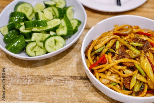 Goshilik lagman, a Uyghur dish of fresh handmade noodles stir-fried with meat and vegetables with a plate of garlic cucumber salad at Apandim Xinjiang Restaurant in Burwood Chinatown, Sydney, NSW
