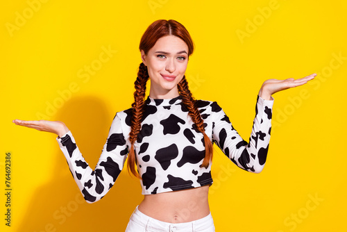 Photo of doubtful thoughtful lady dressed cowskin top comparing arms empty space isolated yellow color background