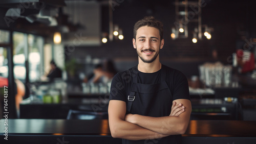 Portrait of a man barista in black t-shirt and apron behind counter in cafe.