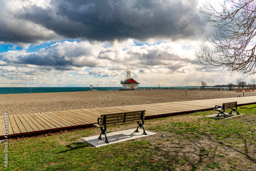 looking out to the horizon past park benches and a wooden boardwalk to a classic wooden lifeguard station in the toronto beaches on a cloudy spring day