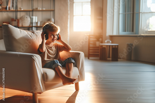 Junge Heranwachsender sitzt barfuß lächelnd auf Sessel Couch helles Wohnzimmer genießt was er hört Musik Gefühle freudig Spaß träumend Rückzug emotional Erholung glücklich geerdet ausgeglichen ruhig 
