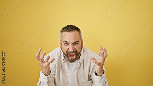 A mature man with grey beard is shouting against an isolated yellow background.