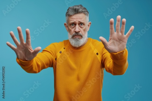 Mature man showing stop gesture expressing fear and defense.