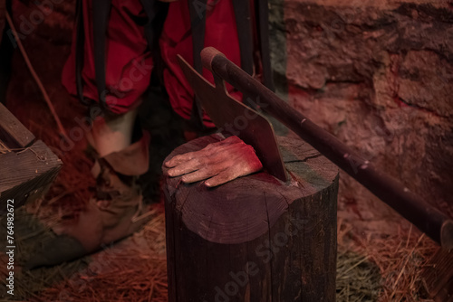 A severed hand by the executioner's ax on a log in the torture chamber.