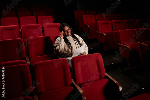 Minimal portrait of smiling African American woman reading lines while sitting in empty audience at theater copy space