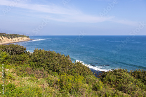 a beautiful spring landscape at Point Dume beach with blue ocean water, lush green trees and plants, homes along the cliffs, waves, blue sky and clouds in Malibu California USA