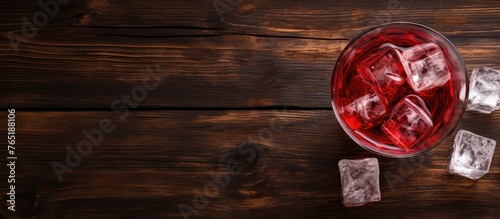 A glass of red wine with ice cubes on a wooden table