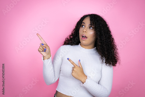 African american woman wearing casual sweater over pink background surprised and pointing her fingers side