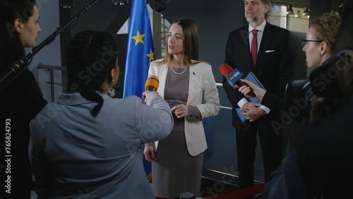 Positive European female politician answers journalists questions, gives interview for media and television in European Parliament building. Representative of the European Union at press conference.