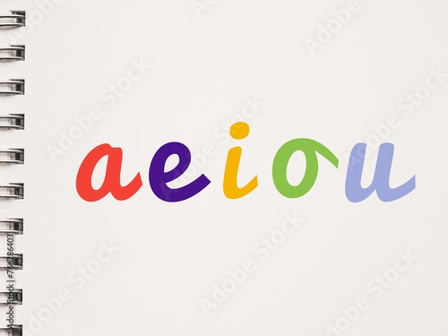 Colorful handwritten AEIOU lowercase vowels on a notebook