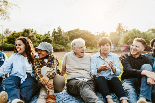 Happy multi generational people having fun sitting on grass in a public park - Diversity and friendship concept