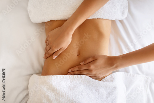 Unrecognizable young woman receiving massage therapy for abdominal area indoor