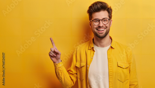 Smiling man with an outstretched index finger, wearing a yellow shirt, against a yellow background.
