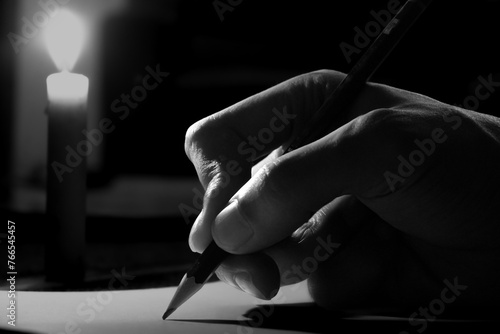 Close up of a man's hand writing on paper at night lit by candlelight, hand writing letter with pencil on paper in candle light condition. writing diary by candlelight in the dark.