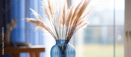Terrestrial plants in electric blue vase on hardwood table, complemented by staple food of dried flowers. Still life photography art capturing the serene event with grass outside the window