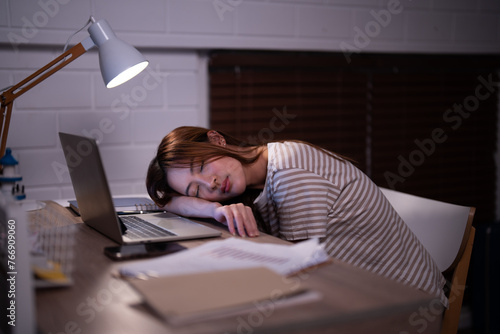 Asian student girl overtaken by fatigue has fallen asleep on their study material after created presentation with the light of a desk lamp illuminated in bedroom at the bedtime