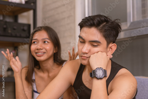 A young asian man looks bored and annoyed, not paying attention to his girlfriends dull and tiresome one-sided chatter. A young lady oblivious to her partner's lack of interest.