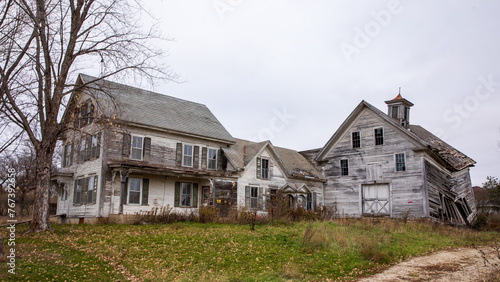 Abandoned home in rural setting. Country estate in ruin. Pale sky over dilapidated buildings in countryside with open tan grassy field. 