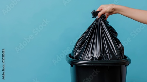 Closeup woman hand throwing away black polyethylene garbage bag on isolated blue background with space for copy