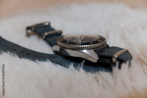 A circular watch with a gray strap on a shaggy carpet.