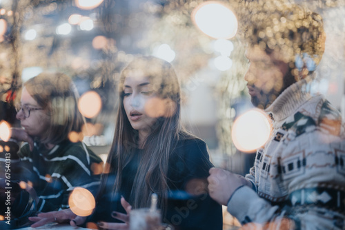 Group of young adults immersed in discussion, captured through a window with warm bokeh lights creating an intimate atmosphere.