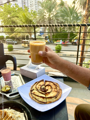 Man holding doodh patti milk tea with chocolate naan sitting on a roof top viewing the city of Karachi, Pakistan.