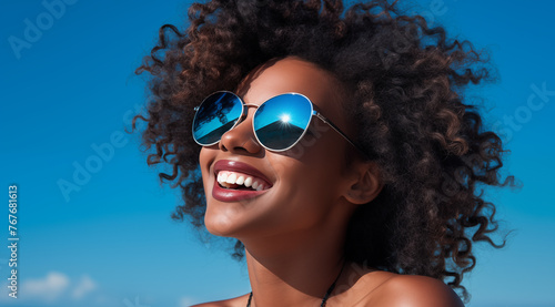 Une belle femme noire, heureuse et souriante portant des lunettes de soleil sous un beau ciel bleu d'été.