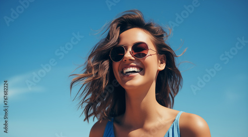 Une belle femme brune, heureuse et souriante portant des lunettes de soleil sous un beau ciel bleu d'été.