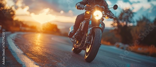A man is riding a motorcycle down a road at dusk. The sun is setting, casting a warm glow on the scene. The motorcycle is equipped with a headlight, illuminating the road ahead