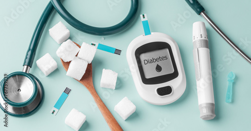 Diabetes concept with blood glucose meter, stethoscope and sugar cube on spoon on green background