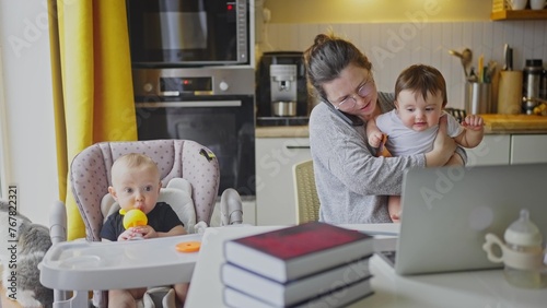 mother working from home remotely with baby daughter in his arms. pandemic remote work business a concept. mother tries to work at home in kitchen, baby children interfere sitting on their fun hands