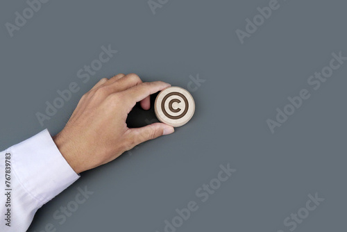A businessman's hand holds a wooden badge with a copyright symbol engraved. Property rights and brand patent protection in business concept.