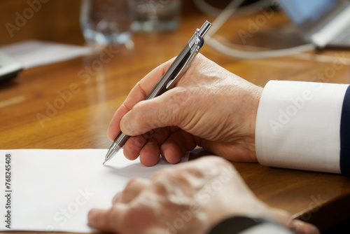 An elderly man in a business suit with cuffs, writing with a fountain pen on a piece of paper. Concept of writing a will or filling out forms. Photo. No face. Selective focus