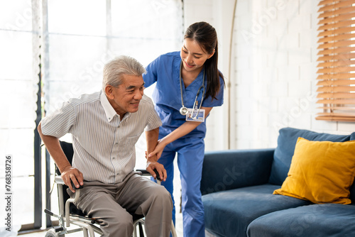 Asian young caregiver take care senior man on wheelchair in house. 