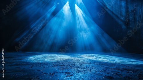 Blue spotlights illuminate an empty stage. The stage is covered in a thin layer of water, which reflects the light and creates a shimmering effect.