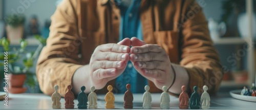 The young man holding hands above the small wooden figures placed on the white desk as a metaphor for protecting human rights and securing the safety of people. Close-up. We all care about each