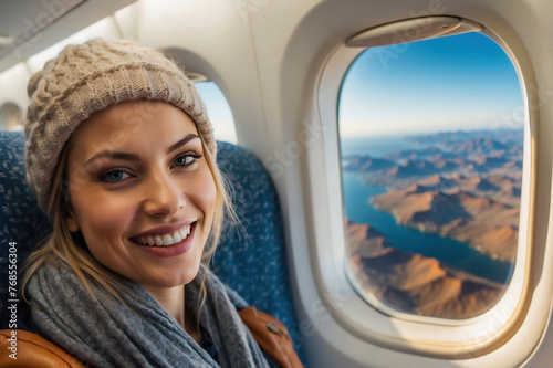 Strahlende junge Frau mit Mütze genießt den Blick aus dem Flugzeugfenster