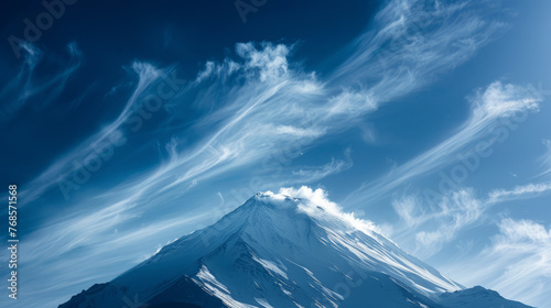 A stunning view of a snow-covered mountain peak beneath a vivid blue sky with artistic brush-like clouds, perfect for nature backgrounds