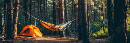 Relaxing in the forest at a campsite, a hanging hammock hangs on the trees near the tents in the rays of the setting sun, banner