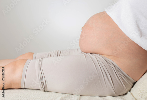 A pregnant girl with a big belly sits against a white wall. Concept of testing amniotic fluid to check for genetic diseases in the fetus, amniocentesis. Copy space for text, preparation for childbirth