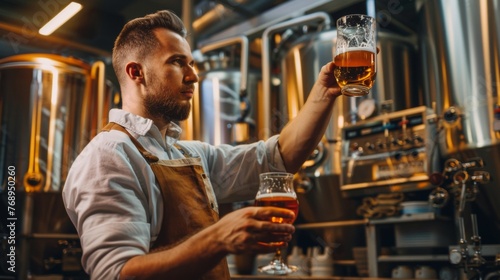 Expert brewer in apron holds glass of craft beer and checking quality and color. Worker man sommeliers taste drink on brewery factory.