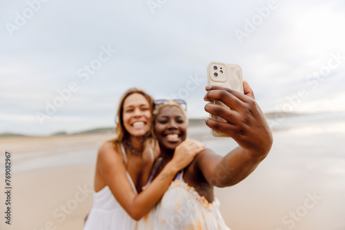 two friends having a good time on the beach taking selfie pictures with their smart phone during a summer trip